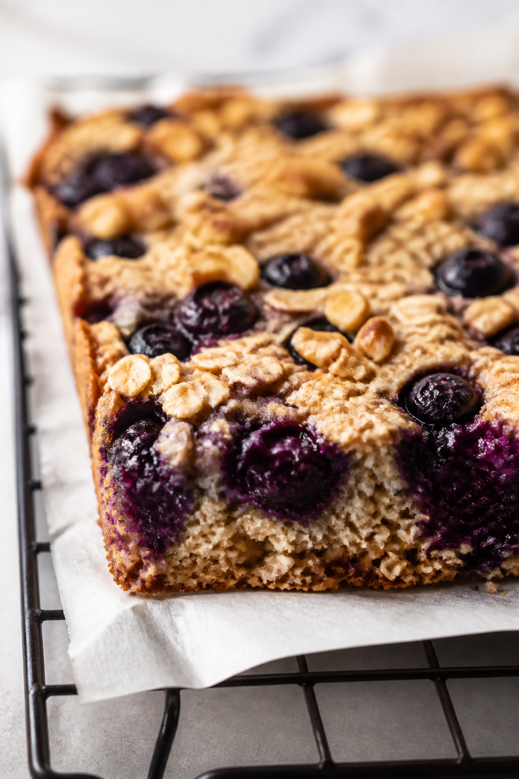 Close-up detail: Freshly baked blueberry oat bar slab just out of the pan, edges lightly golden and 