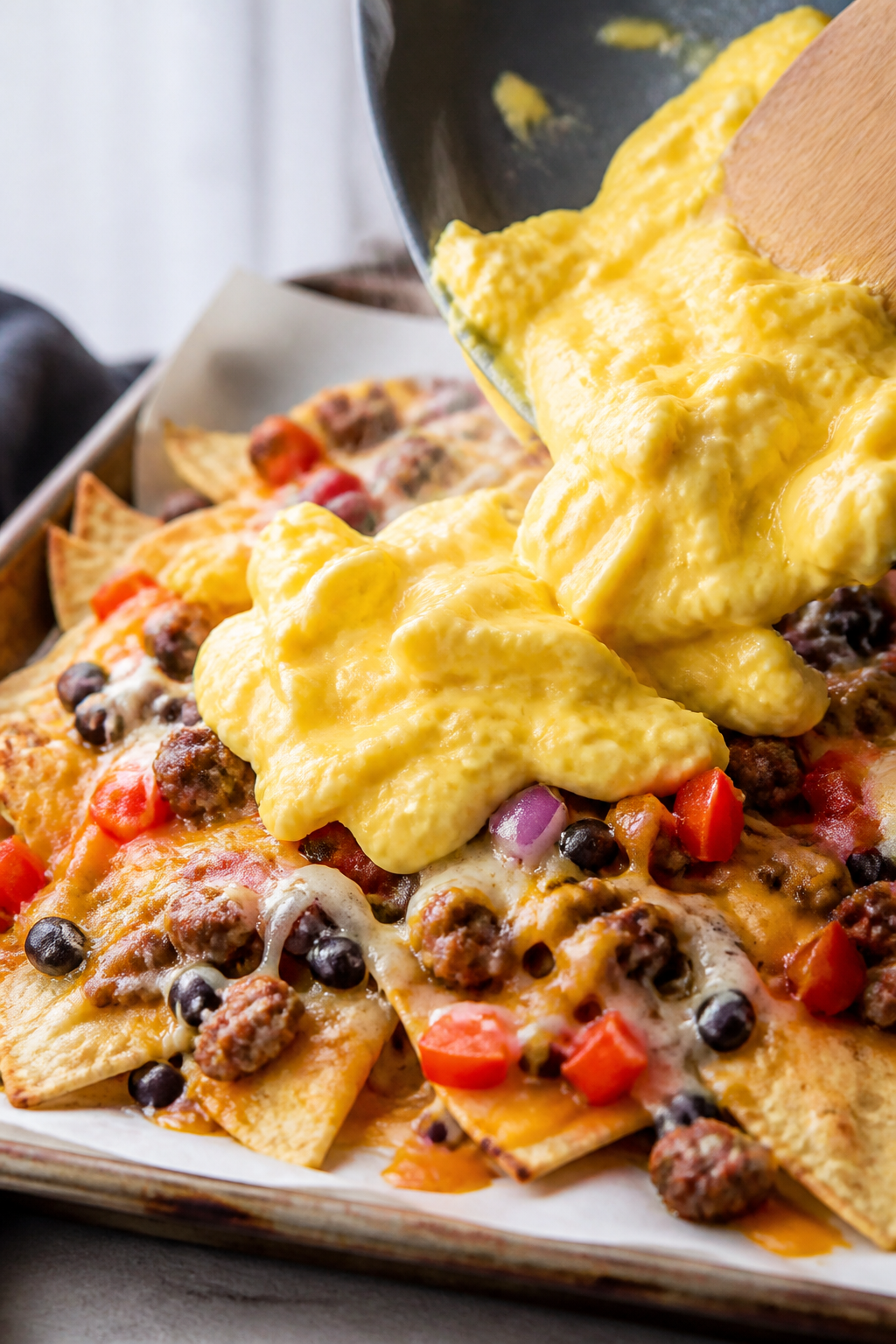 Close-up detail: Soft-scrambled eggs just set and glossy, being gently folded onto a sheet pan of me