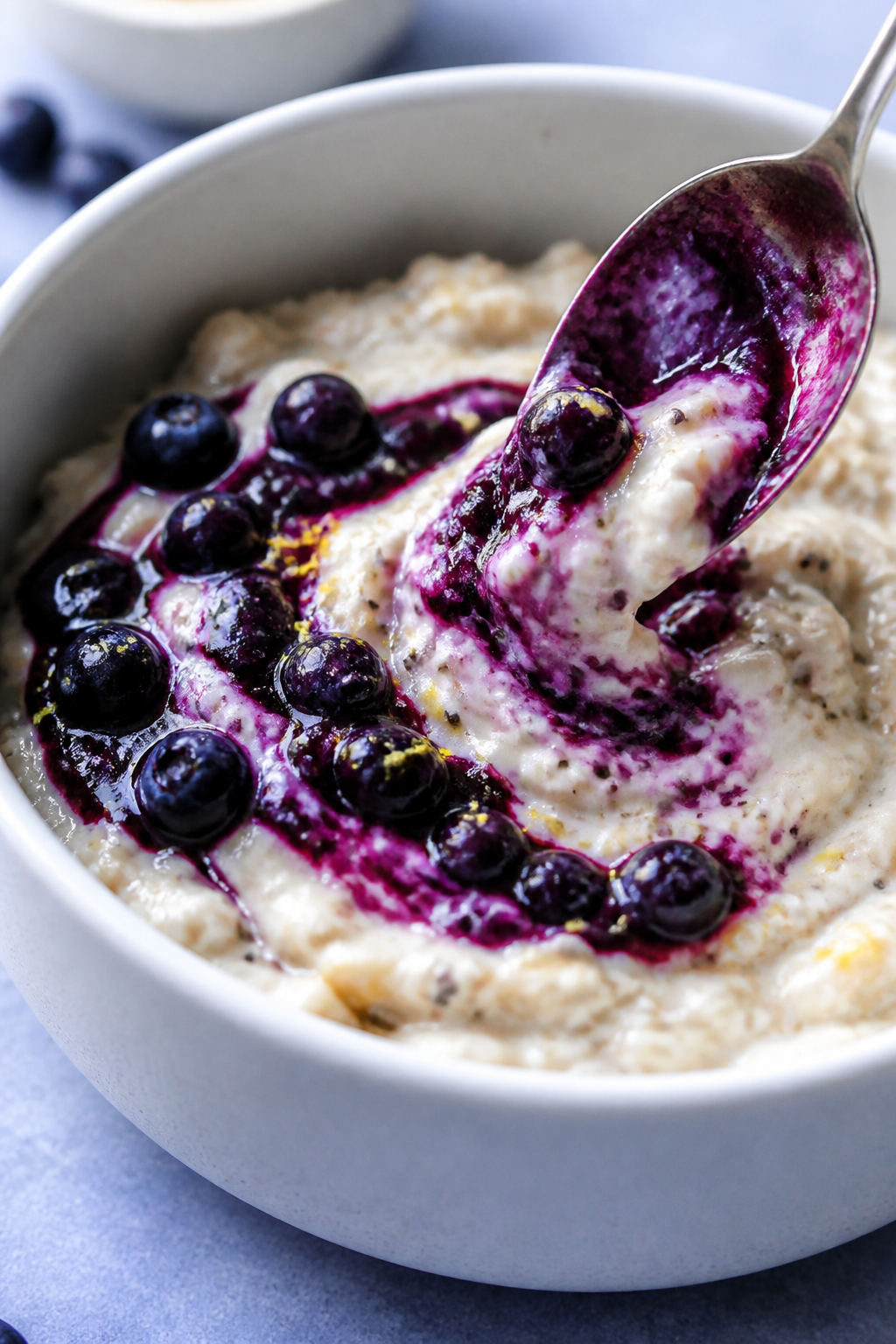 Close-up detail: Warm blueberry compote being spooned and gently swirled into creamy cheesecake oats
