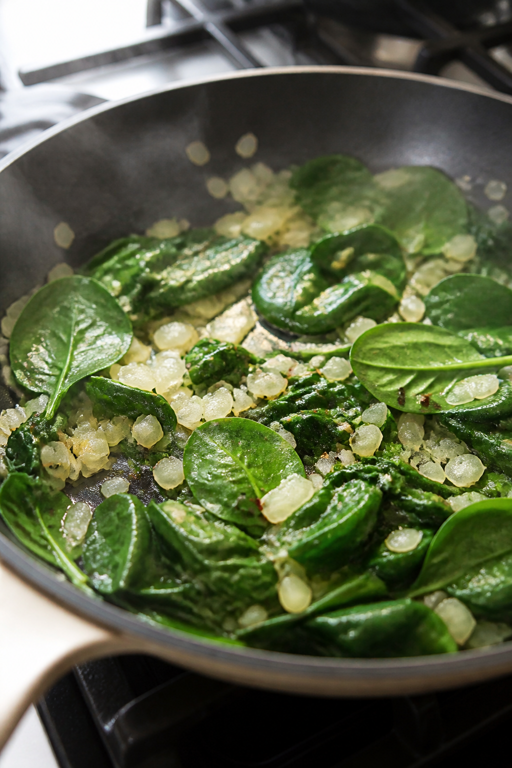 Cooking process — Sauté and wilt: Close-up of a skillet scene showing translucent diced onions an