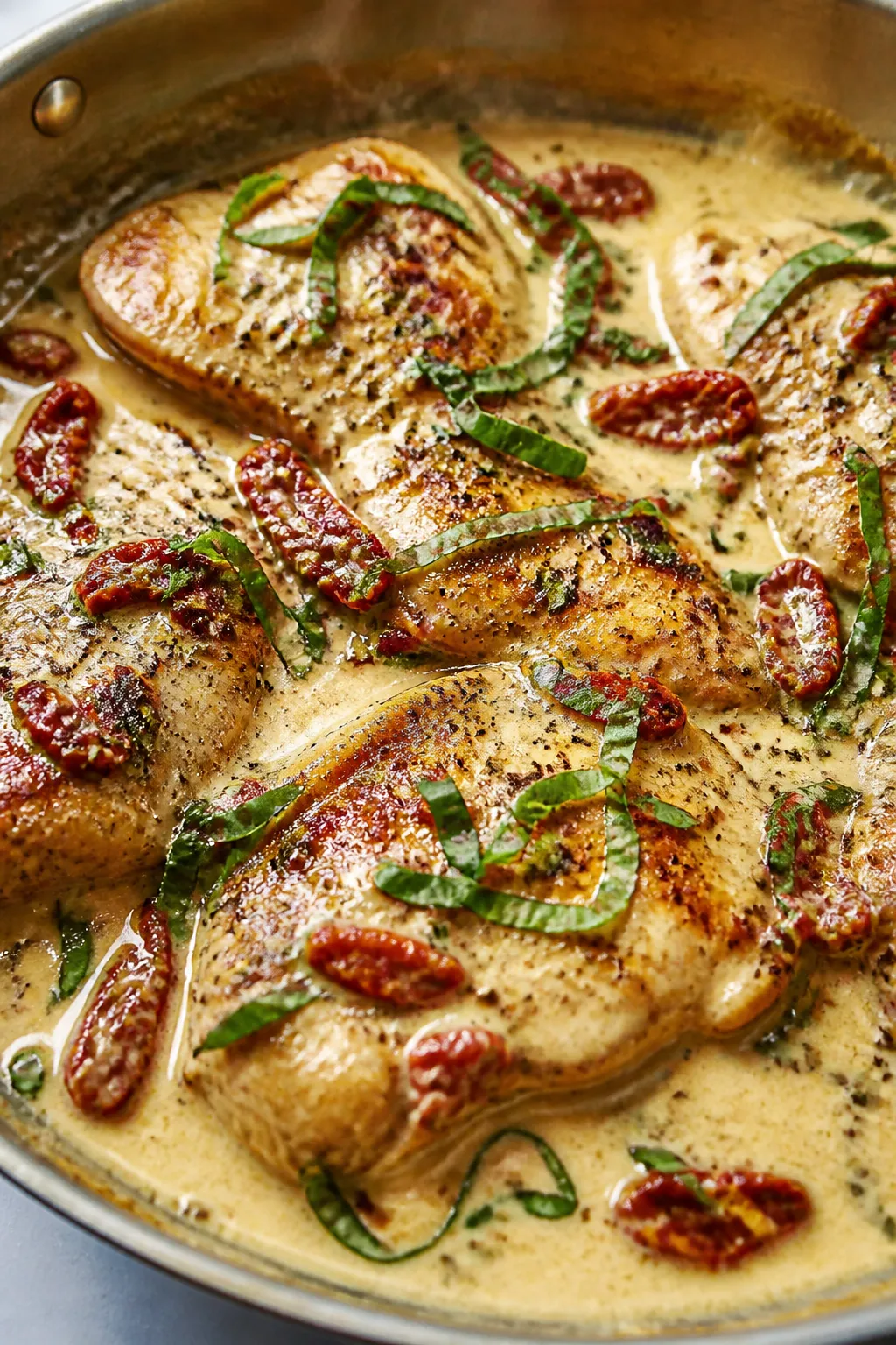 Close-up detail: Golden-brown chicken cutlets simmering in a creamy garlic-Parmesan sauce with chopp
