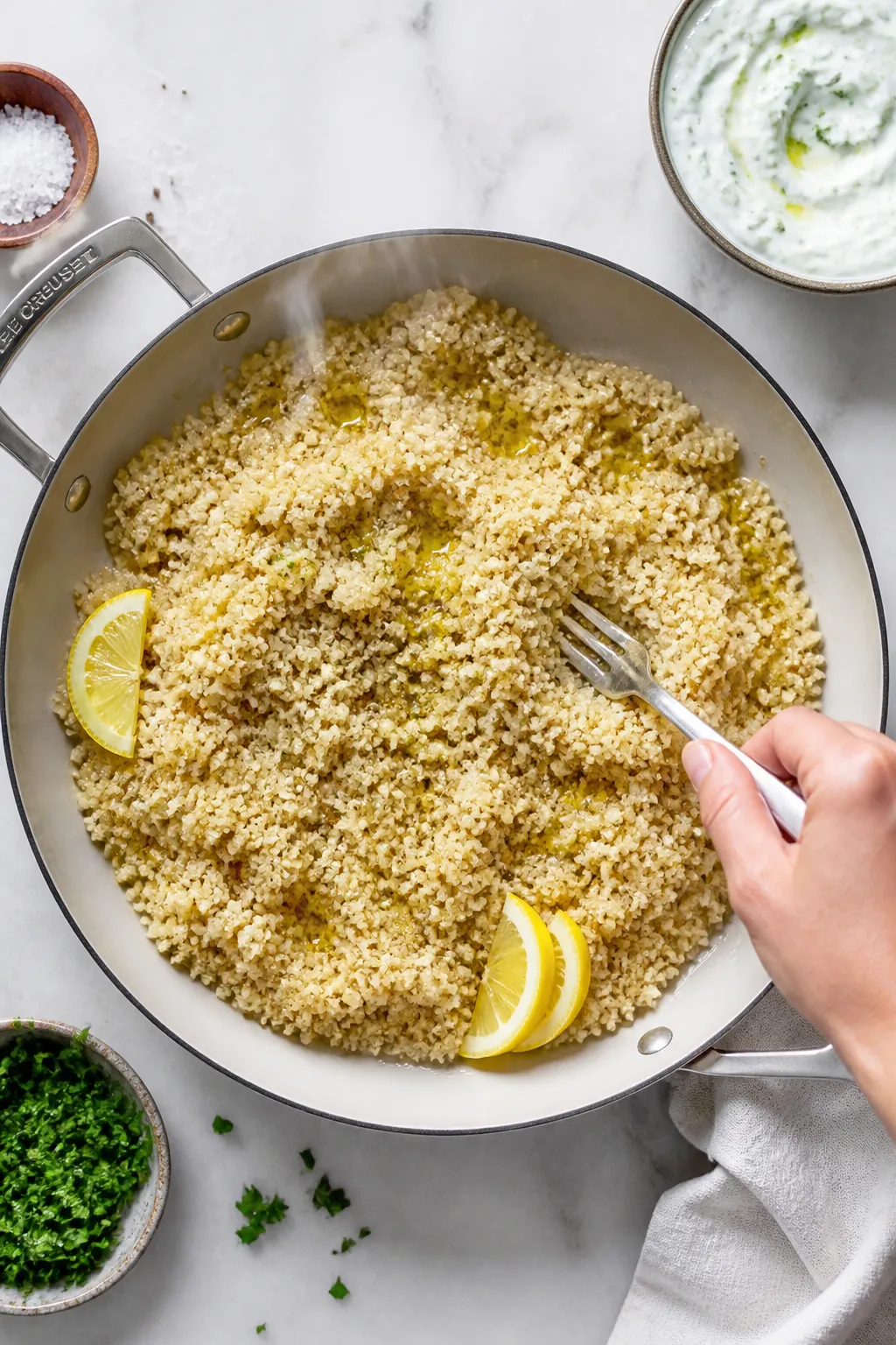 Cooking process: Overhead shot of fluffy quinoa being fluffed with a fork in a wide, shallow pan, st