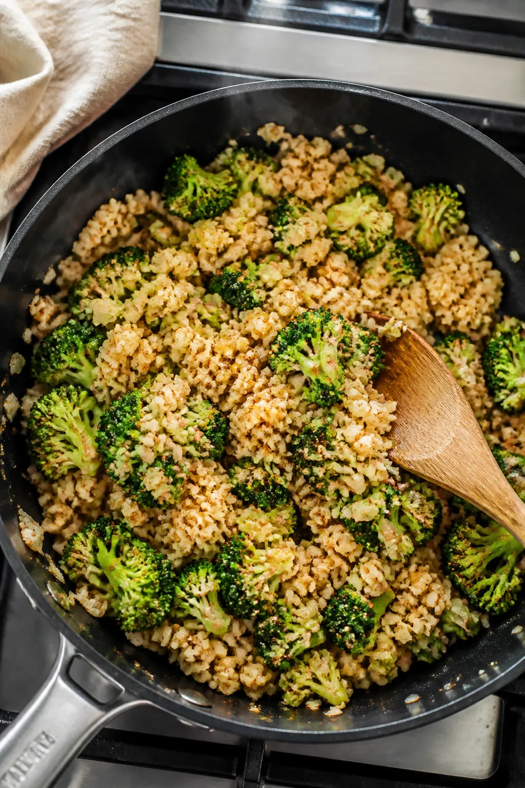 Cooking process: Overhead shot of the sauté step in a wide skillet—riced cauliflower and small br